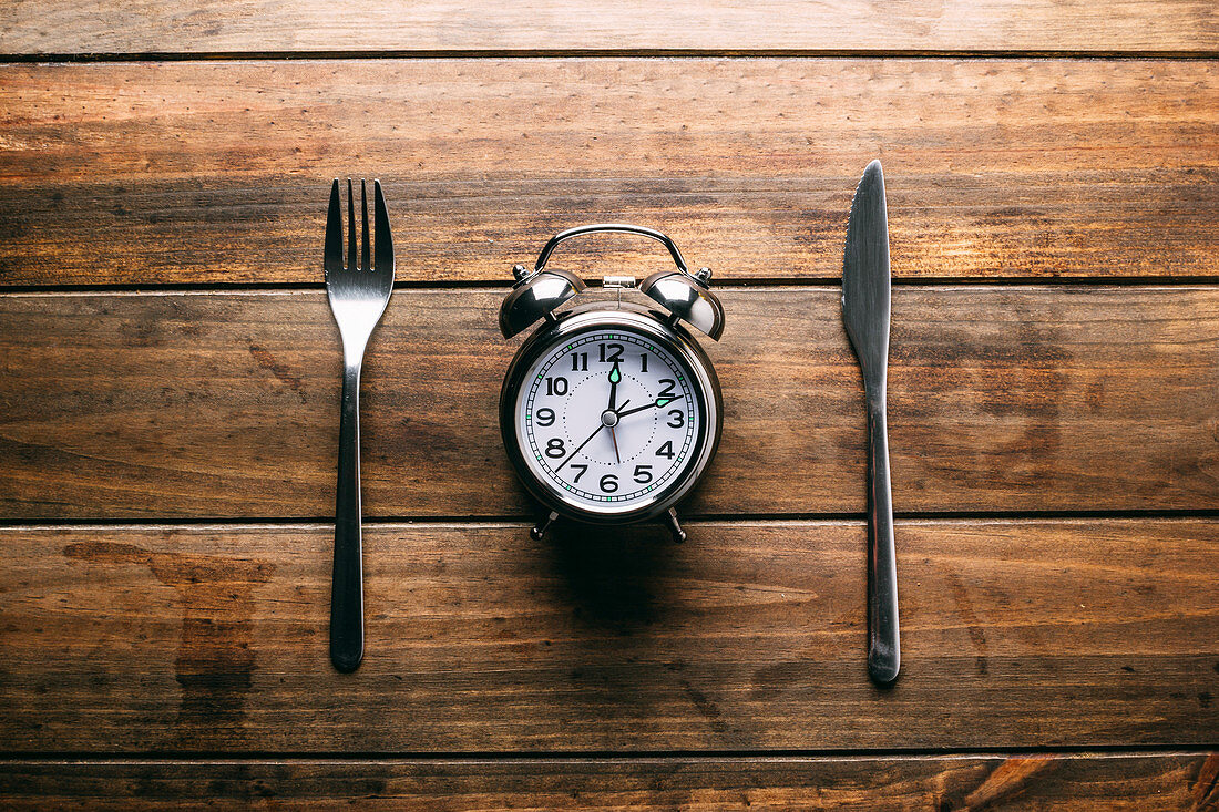 Fork and knife lying on wooden tabletop near mechanical alarm clock
