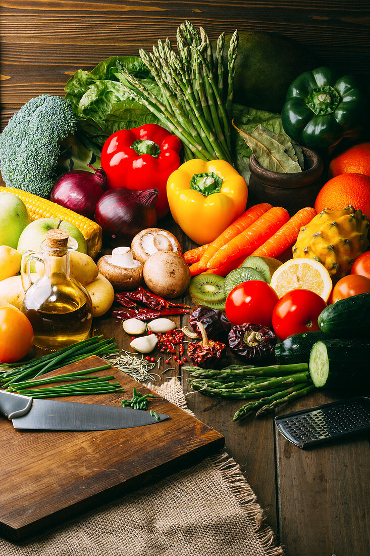 Assorted fresh vegetables and bottle of oil lying on timber tabletop near various cooking tools