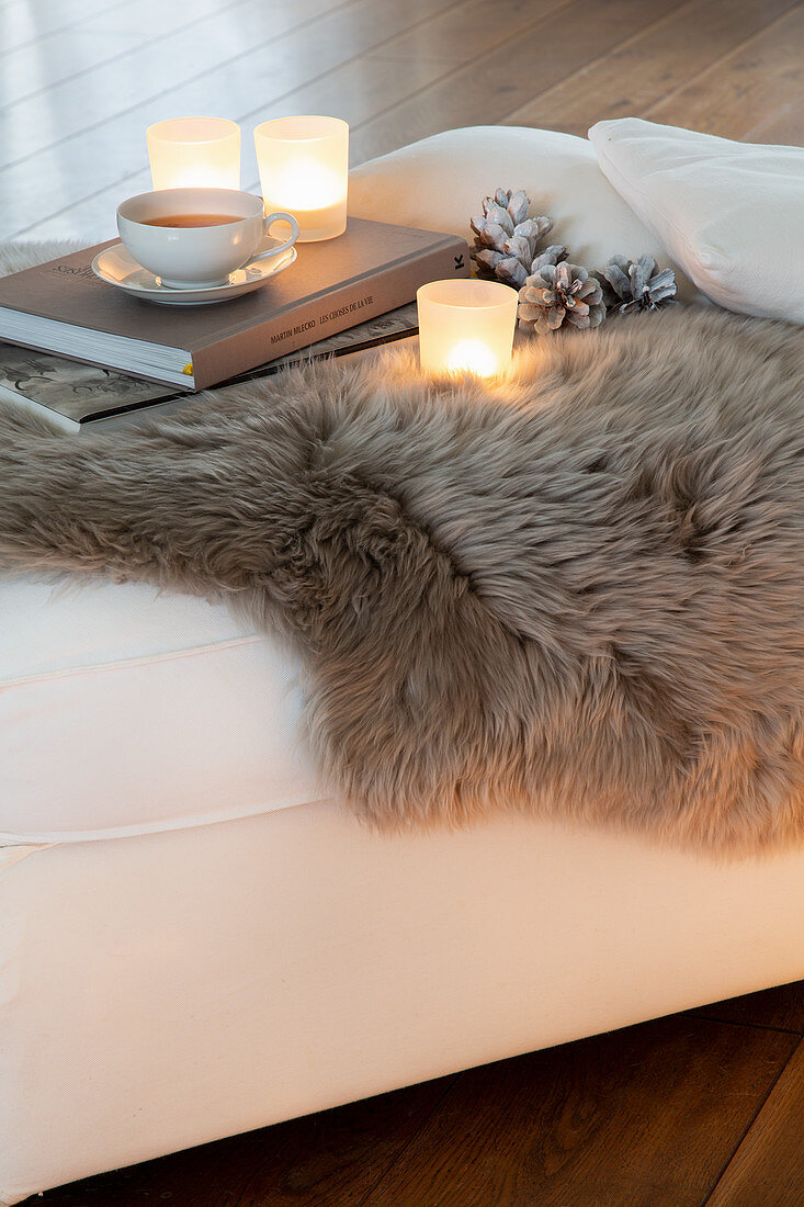 Tealights, books and cup of tea on fur blanket