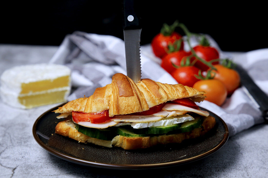 A croissant sandwich with cucumber, cheese, sausage and tomatoes