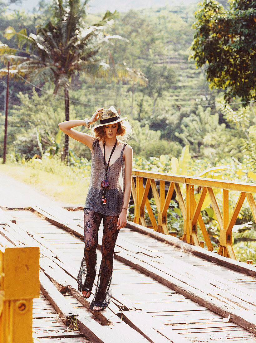 A young blonde woman wearing see-through trousers and a shirt with a hat and a necklace