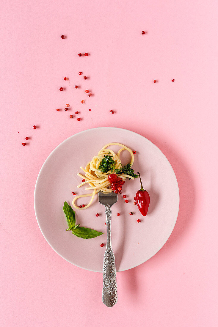 Spaghetti with tomato and pesto sauce on pink background