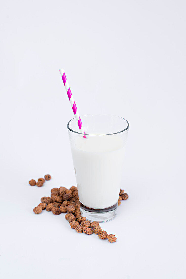 Heap of tasty raisins lying near glass with fresh milk and striped straw on white background