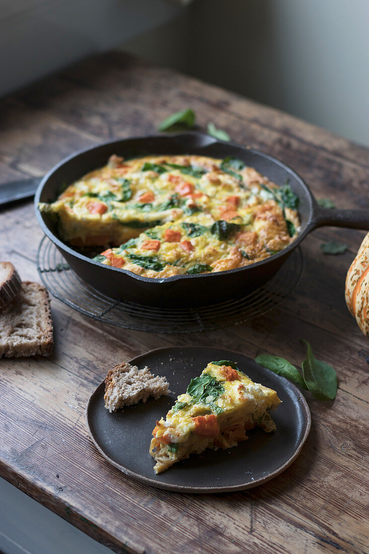 Plate and metal saucepan with delicious pumpkin and spinach frittata standing on timber tabletop