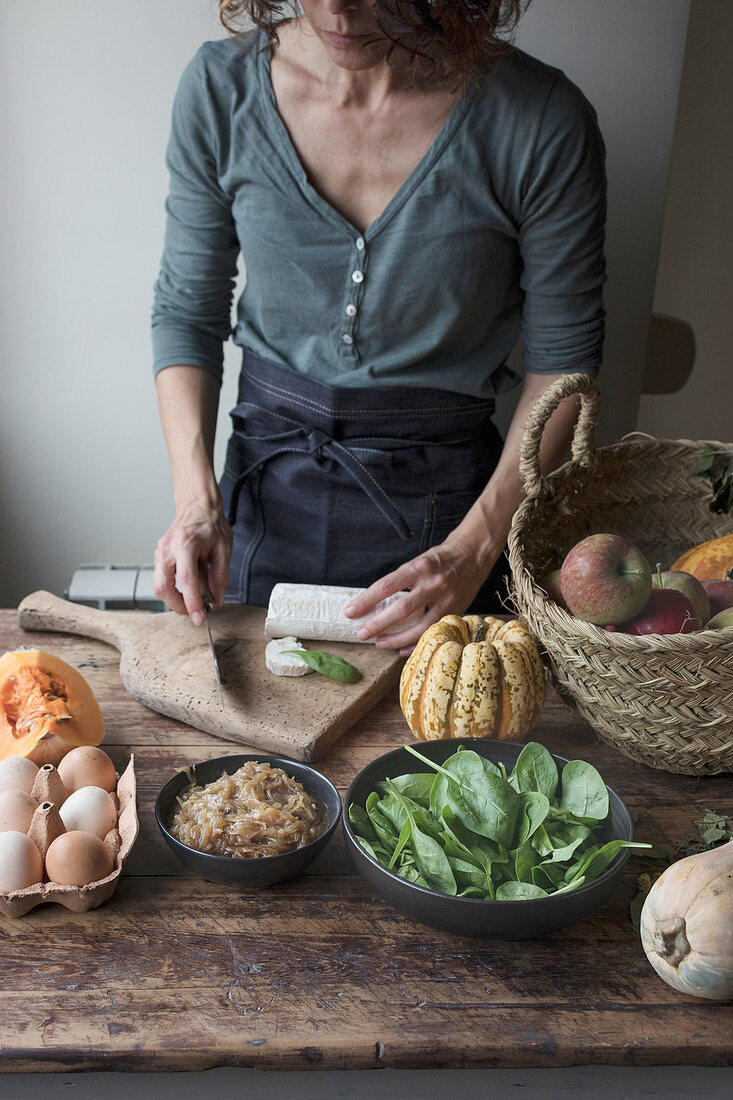 Woman cutting ingredients for tasty pumpkin and spinach frittata while standing near wooden table