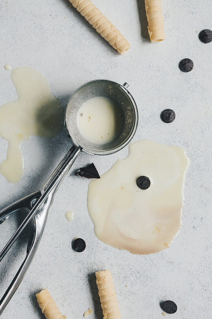 Zerlaufene Eiscreme, Waffelröllchen, Schokoplättchen und Éisportionierer