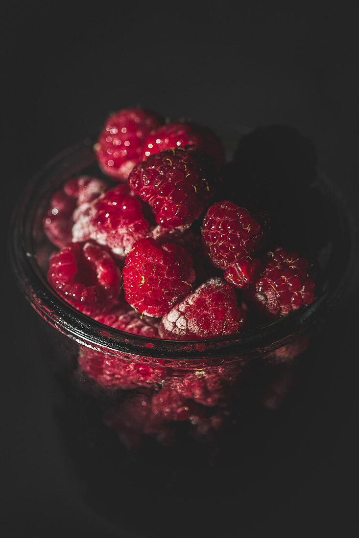 Yummy ripe raspberries lying in glass jar in dark room