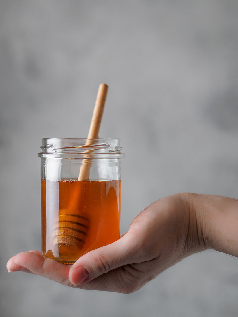 Honig im Glas mit Honigheber auf Frauenhand