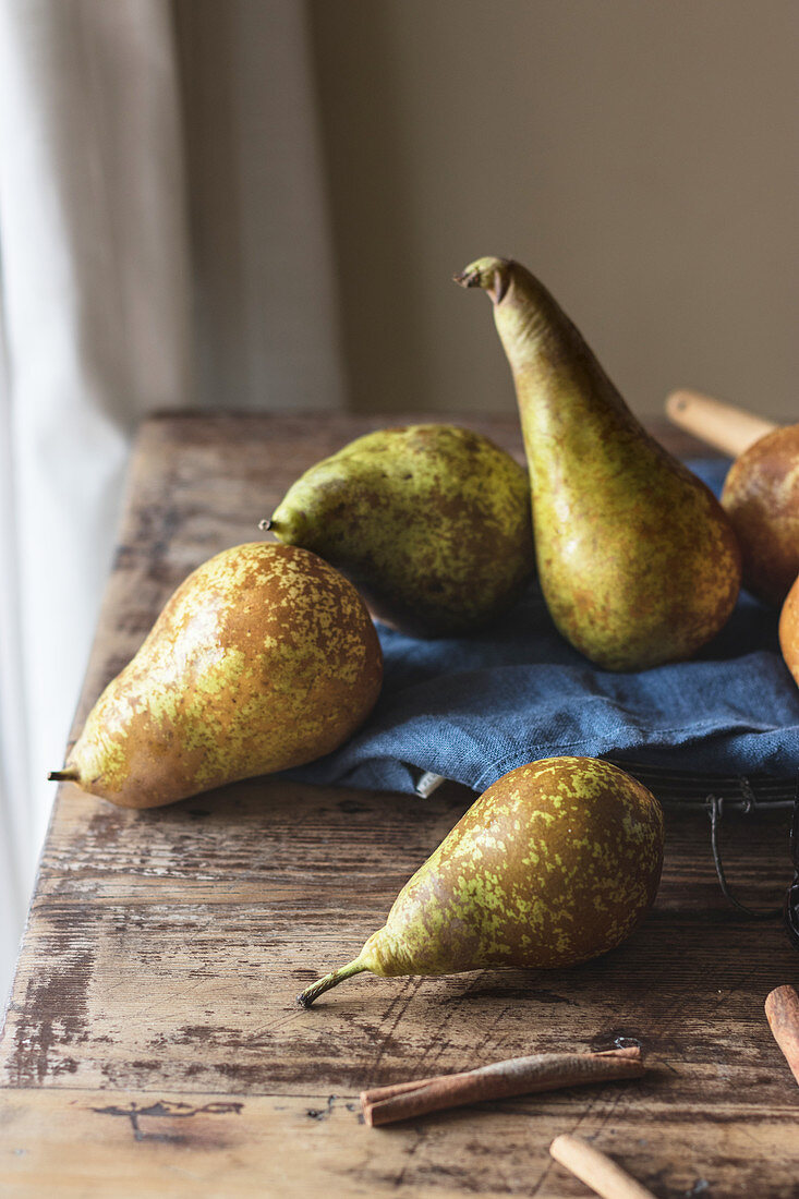 Sticks of aromatic cinnamon and fresh pears lying on lumber table in kitchen