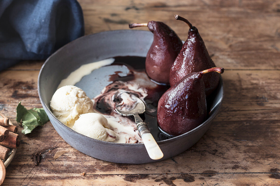 Small spoon lying in metal bowl with melting ice cream and tasty pears in wine