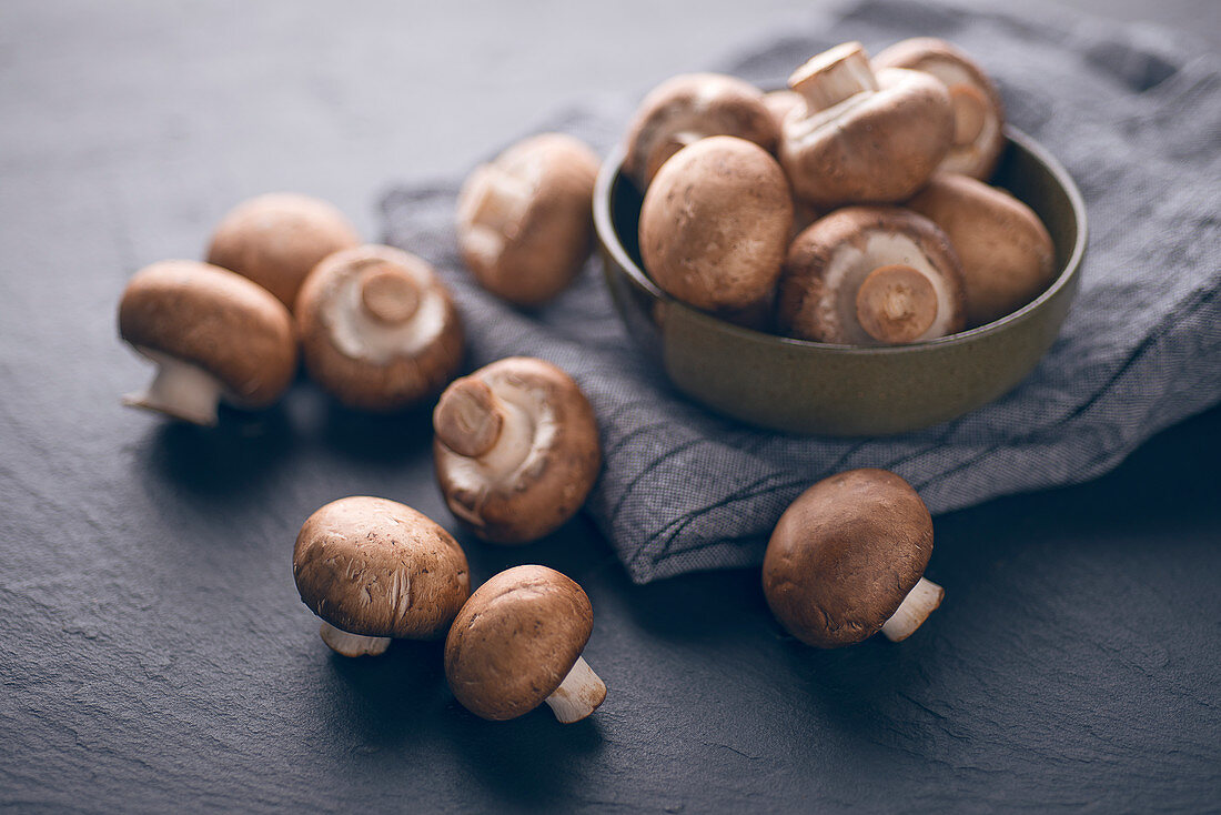 Frische braune Champignons im Schälchen und auf Schieferuntergrund