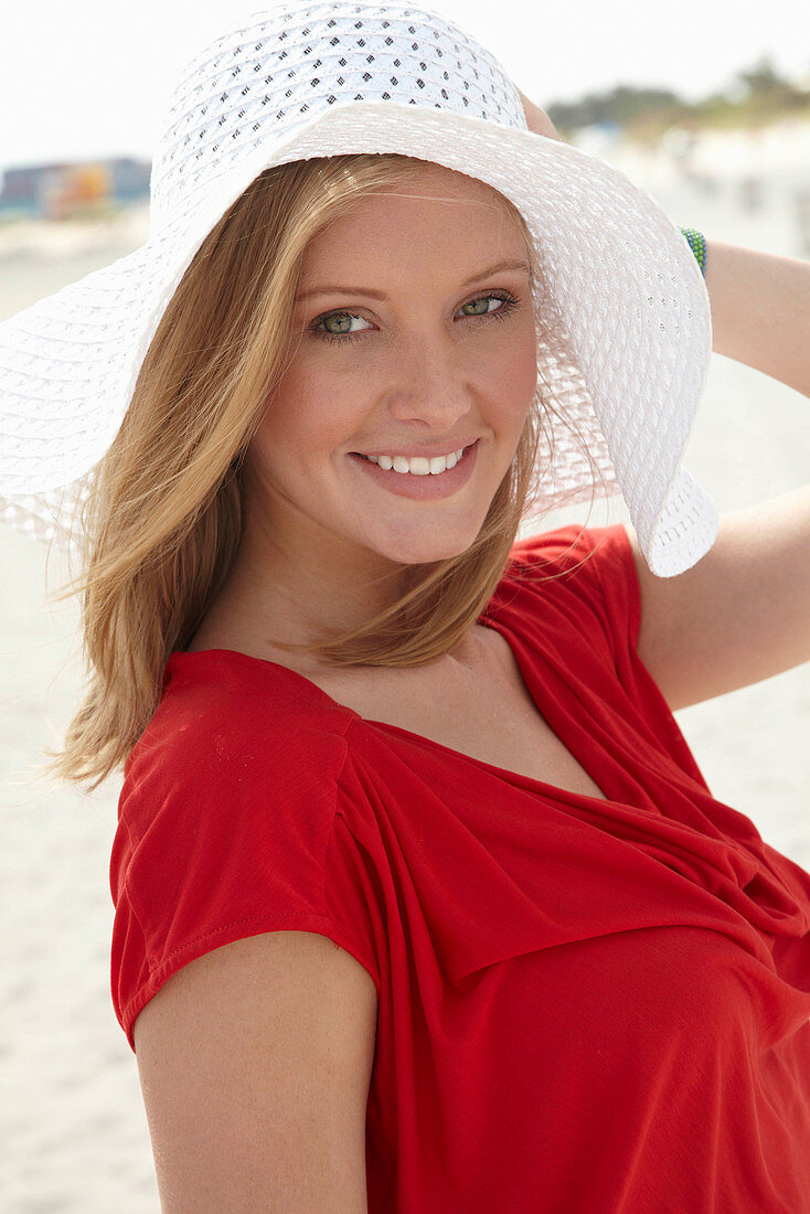 A blonde woman on a beach wearing a red top and a white hat