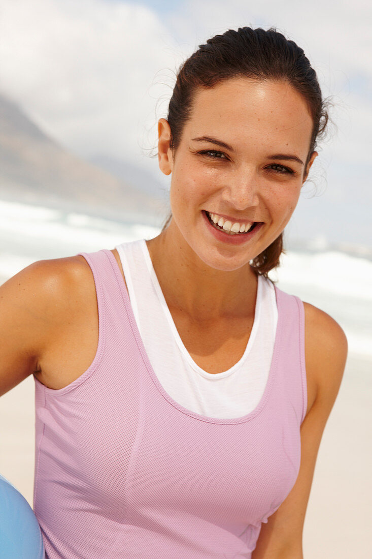 A young brunette woman by the sea wearing sports clothes with a ball