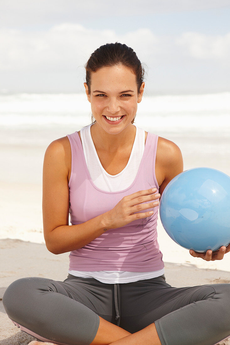 Junge brünette Frau mit Ball im Lotussitz am Meer