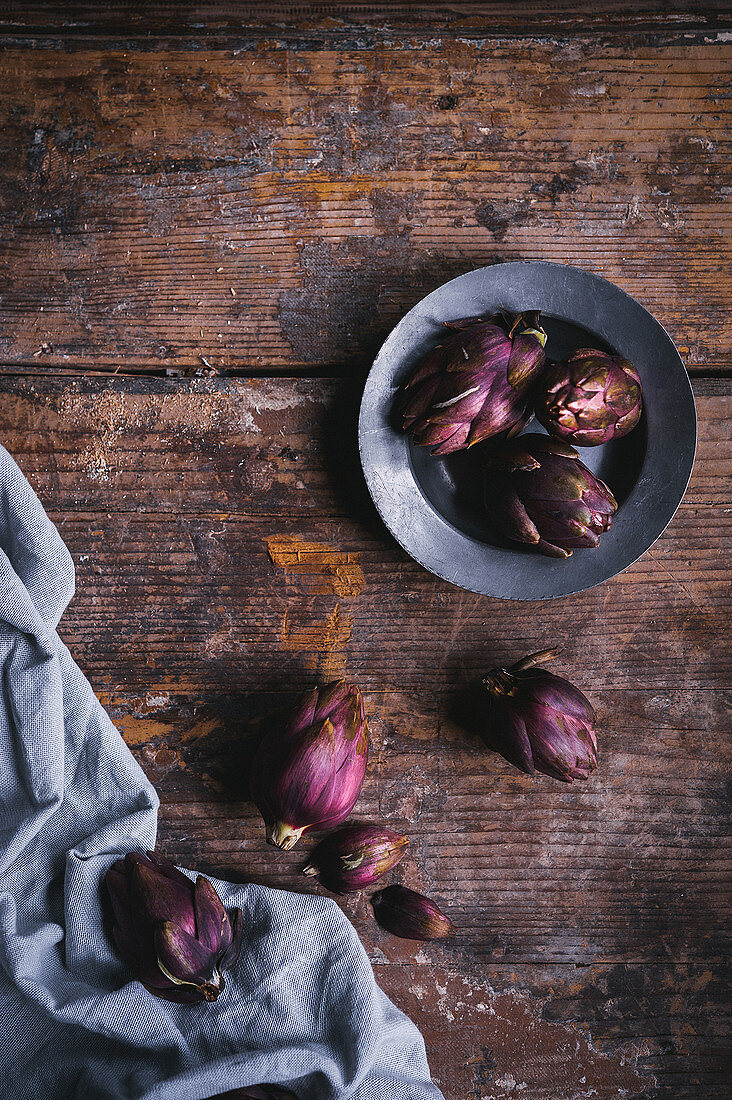 Small violet artichokes on a cloth and a wooden surface