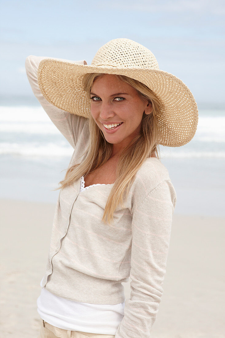 Blonde Frau mit Sommerhut in hellem Cardigan und Shorts am Strand