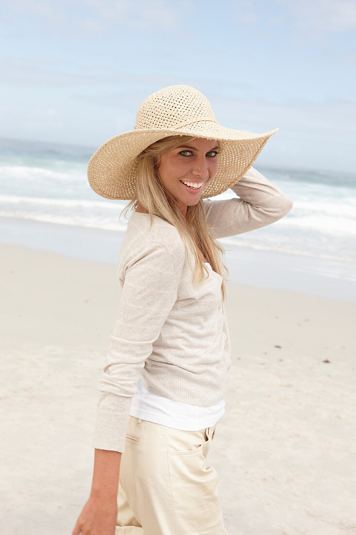 Blonde Frau mit Sommerhut in hellem Cardigan und Shorts am Strand