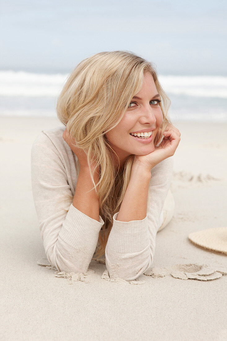 A blond woman on a beach wearing a light cardigan