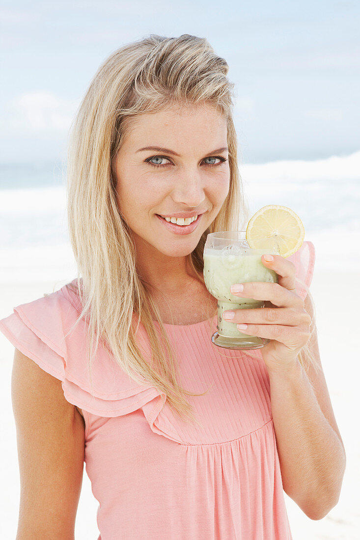 Junge Frau mit Smoothie im rosa Top am Strand