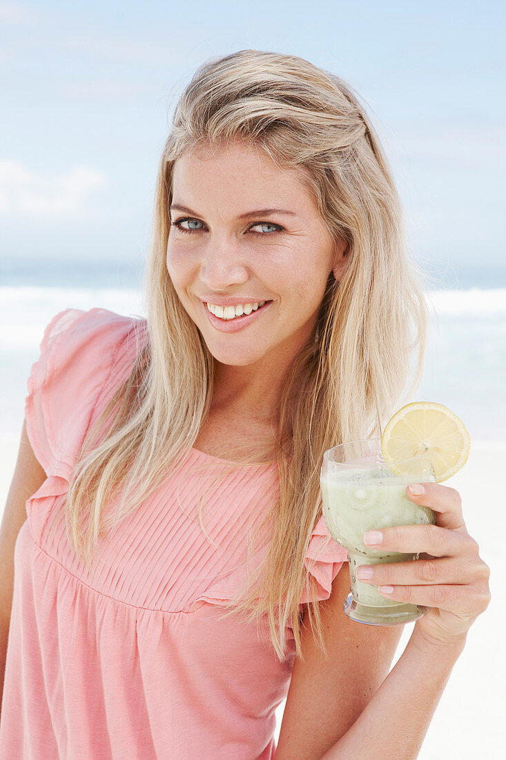 A young woman on a beach with a smoothie wearing a pink top