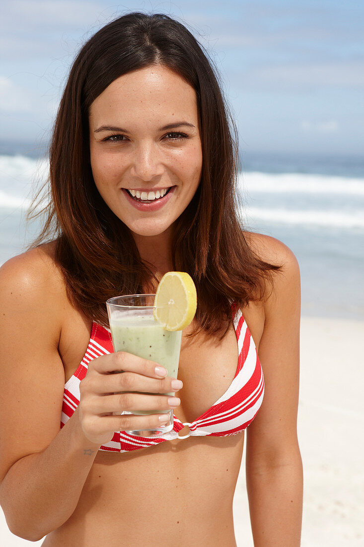 Junge brünette Frau mit Smoothie im Bikinoberteil am Strand