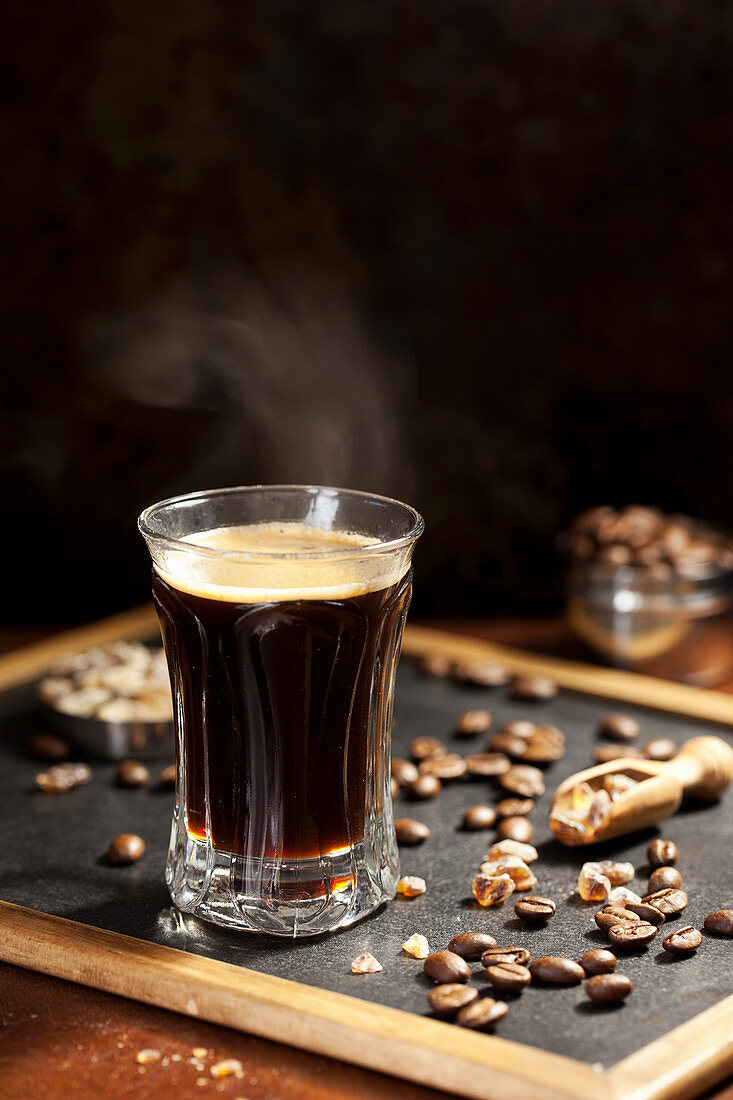 Steaming black coffee with coffee beans