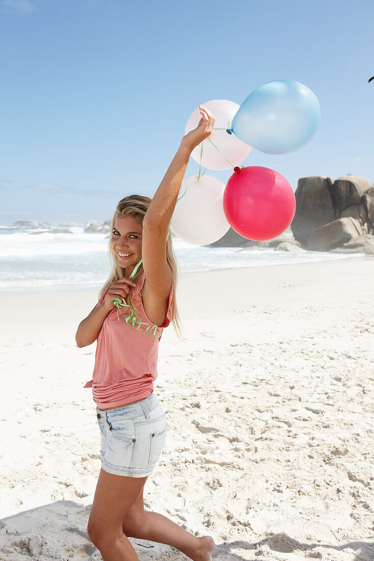 Junge Frau mit Luftballons im rosa Top und Jeansshorts am Strand