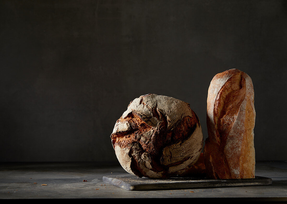 Crusty bread and a baguette in front of a dark background