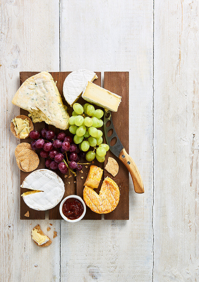 Selection of soft cheeses with biscuits, grapes and chutney on a brown wooden board