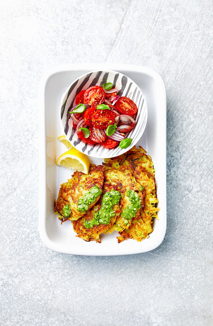 Potato and zucchini fritters served with green pesto and tomato salad