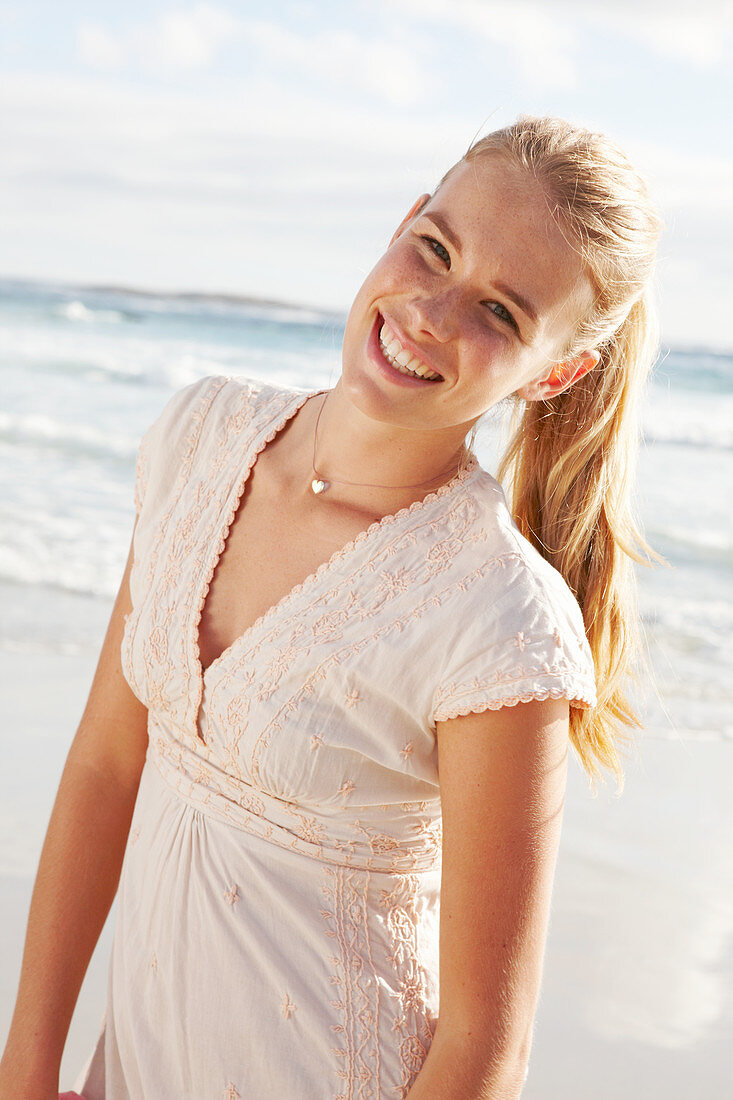 Blonde Frau in weißem Kleid mit Stickerei am Meer