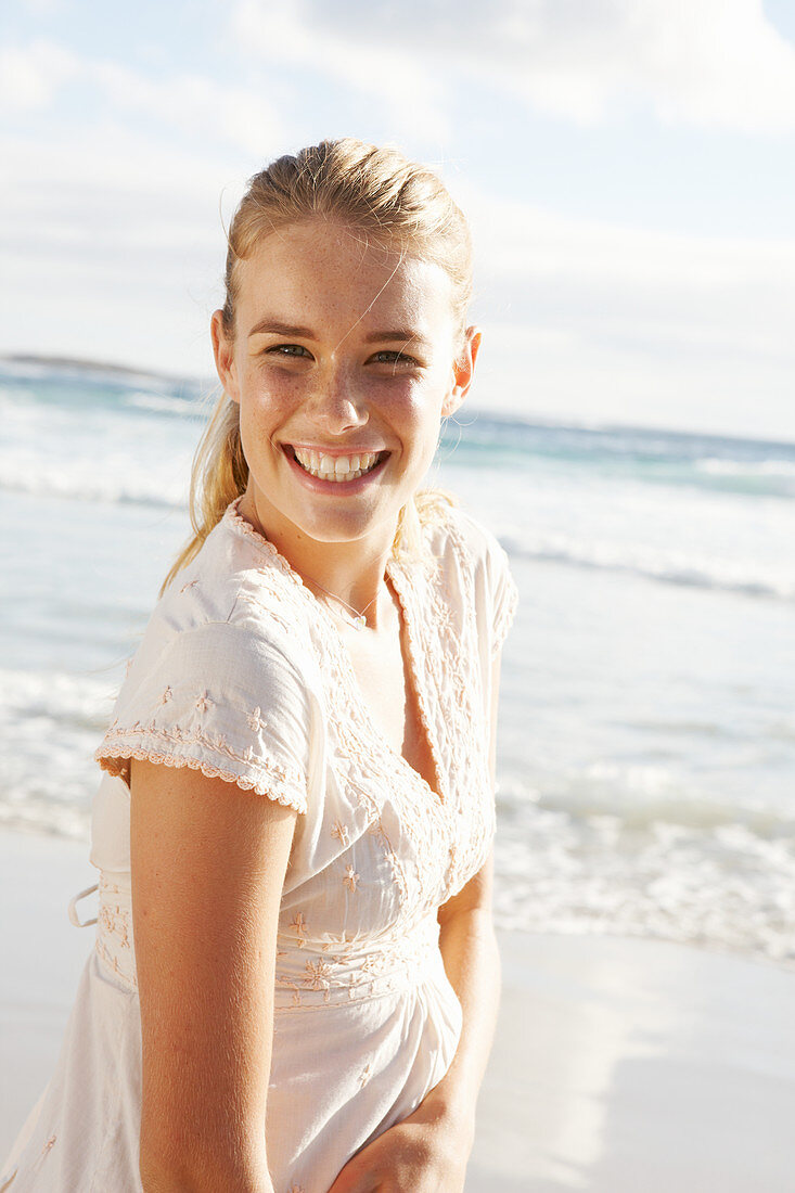 Blonde Frau in weißem Kleid mit Stickerei am Meer