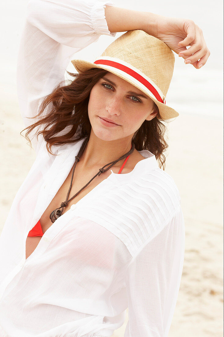 A brunette woman wearing a hat, a red bikini top and a white blouse