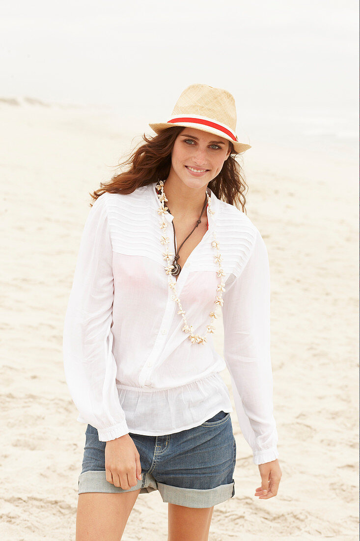 A brunette woman wearing a hat, a white blouse and denim shorts