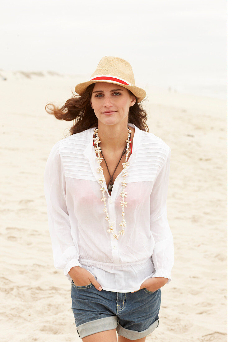 A brunette woman wearing a hat, a white blouse and denim shorts