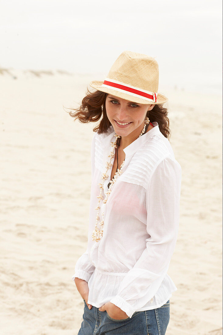 A brunette woman wearing a hat, a white blouse and denim shorts