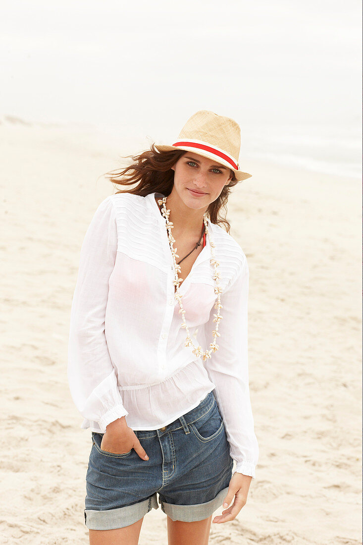 A brunette woman wearing a hat, a white blouse and denim shorts