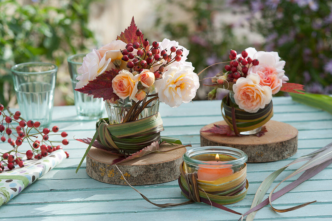 Kleine Sträuße aus Rosenblüten,  Hagebutten und Herbstlaub mit Chinaschilf