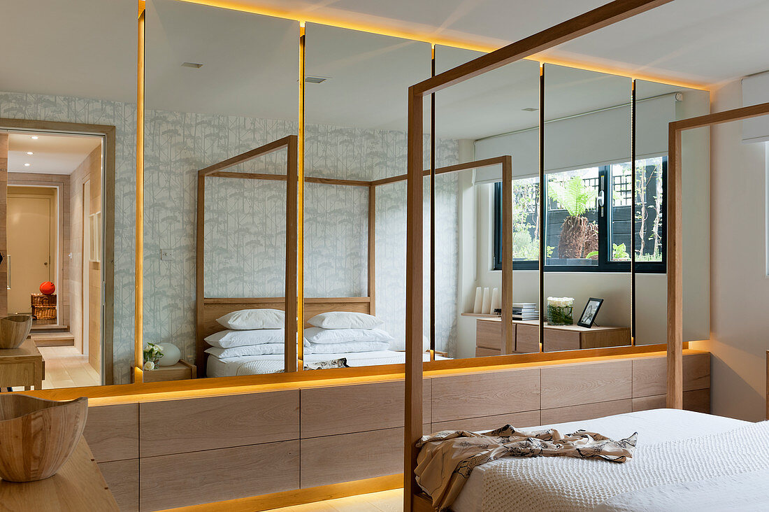 Mirrored, fitted cupboards and modern, wooden, four-poster bed in bedroom