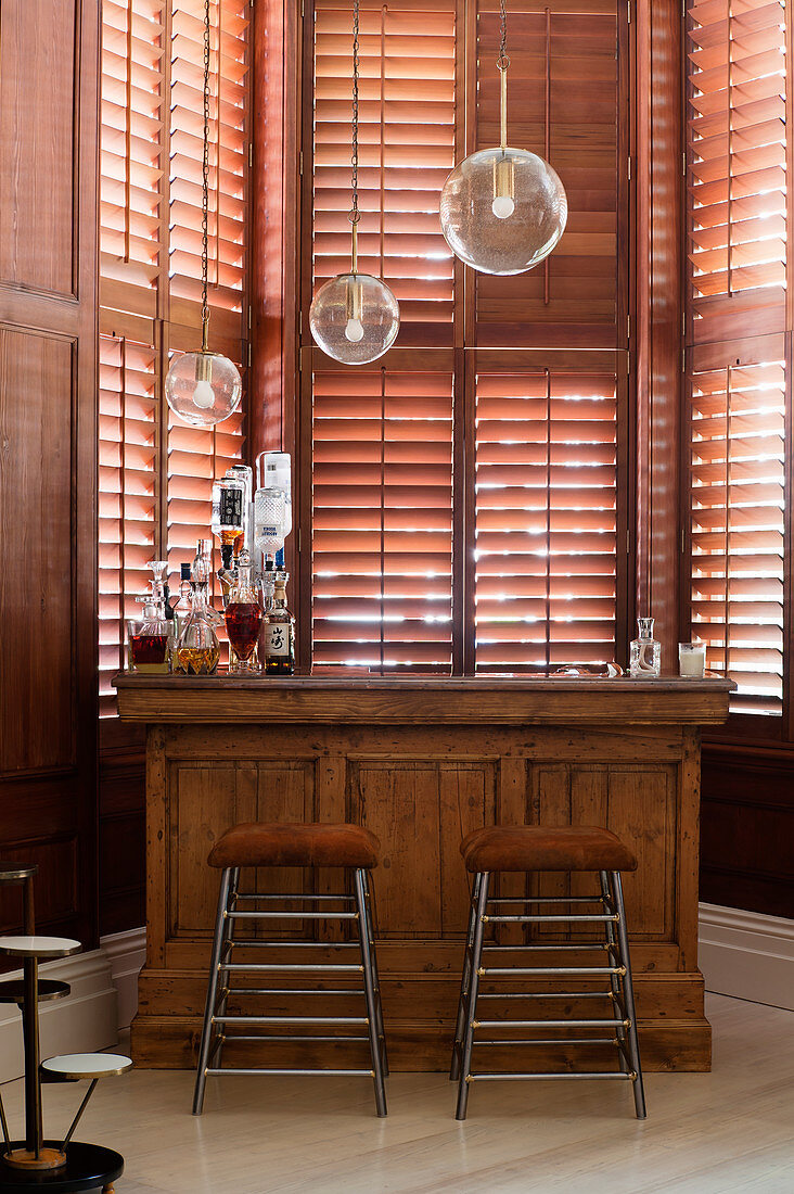 Bar stools at old wooden counter in bay window with shutters