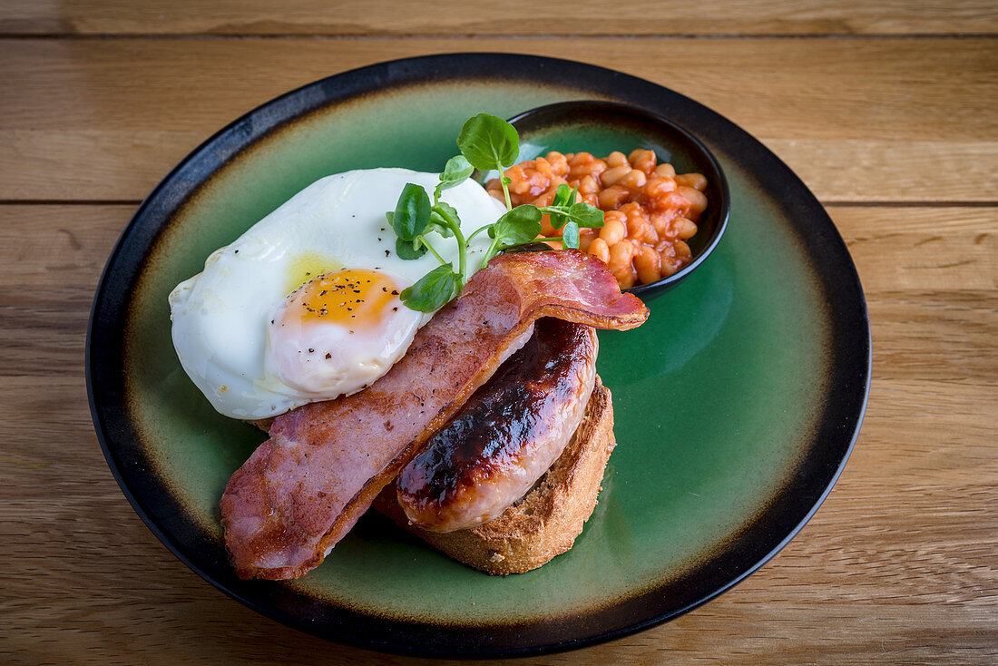 Englisches Frühstück mit Spiegelei, Bratwurst, Bacon und Bohnen