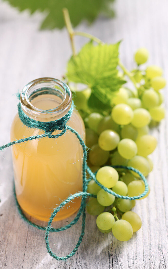 Homemade grape syrup in a glass bottle next to fresh green grapes