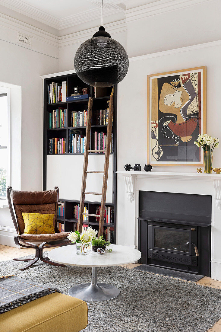 Coffeetable und Klassikerstuhl vor Kamin und Bücherregal mit Leiter im Wohnzimmer