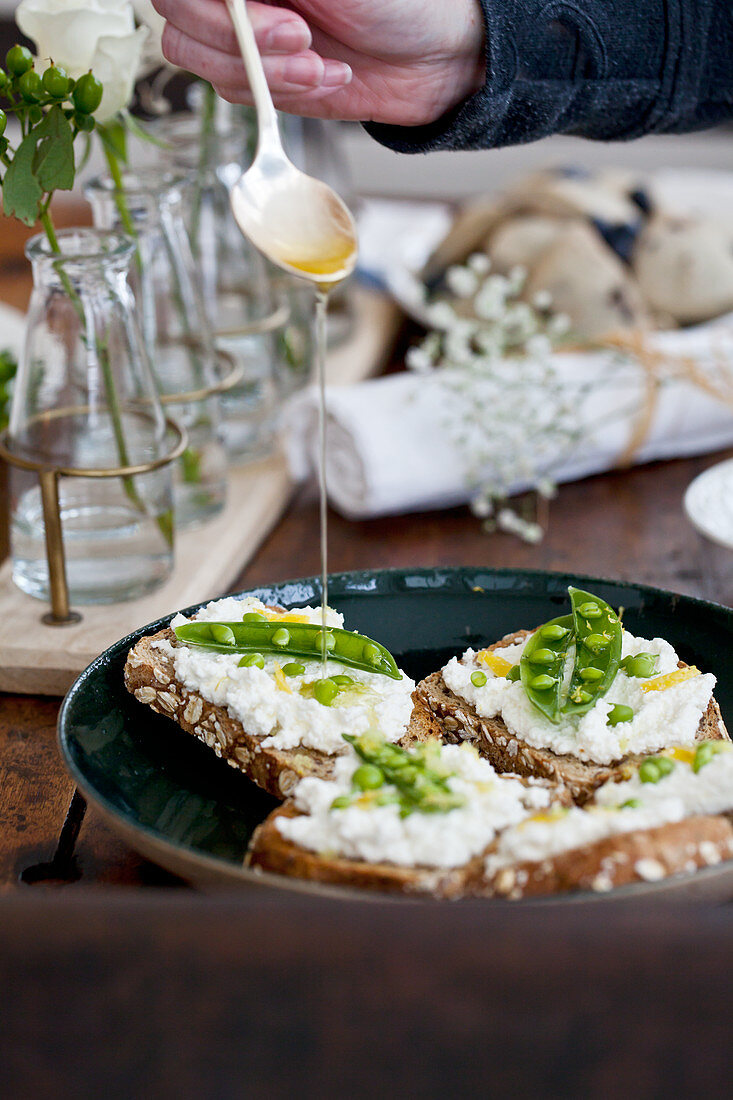 Ricotta toast with peas, lemon zest, and being drizzled with olive oil