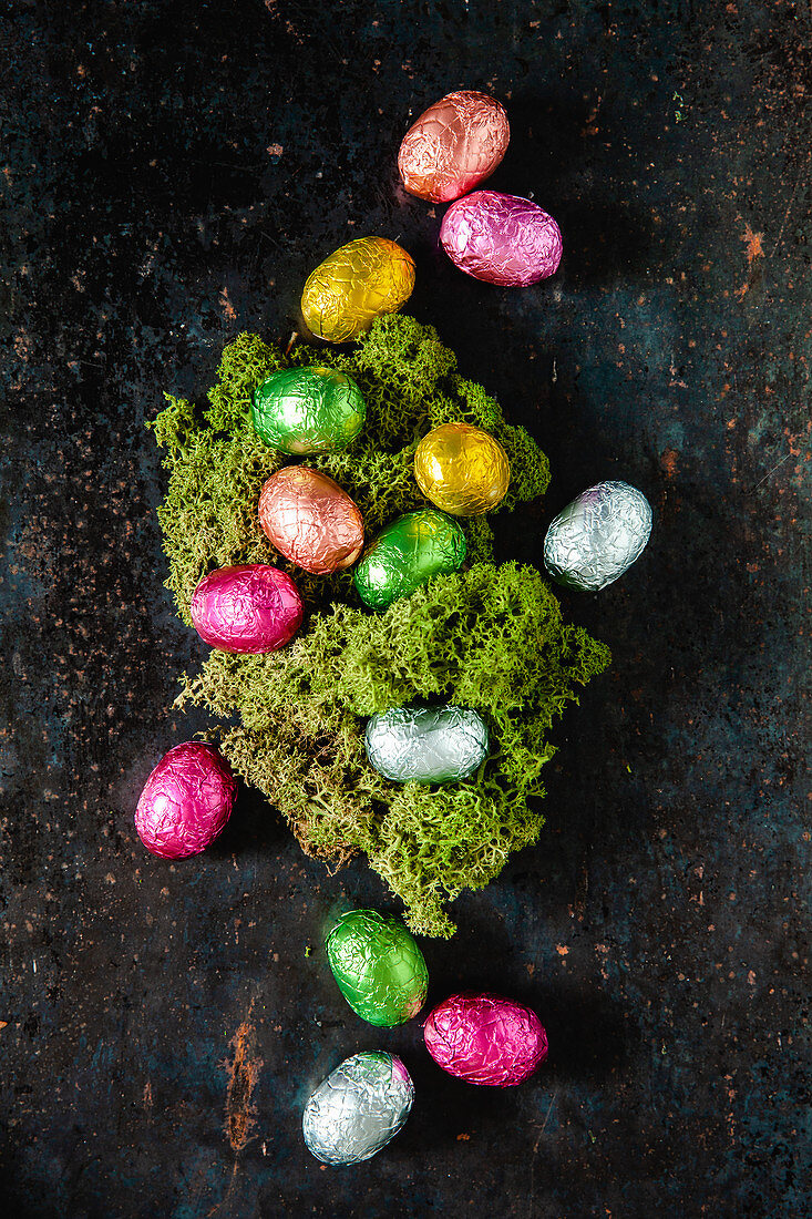 Chocolate eggs wrapped in bright foil surrounding an Easter nest