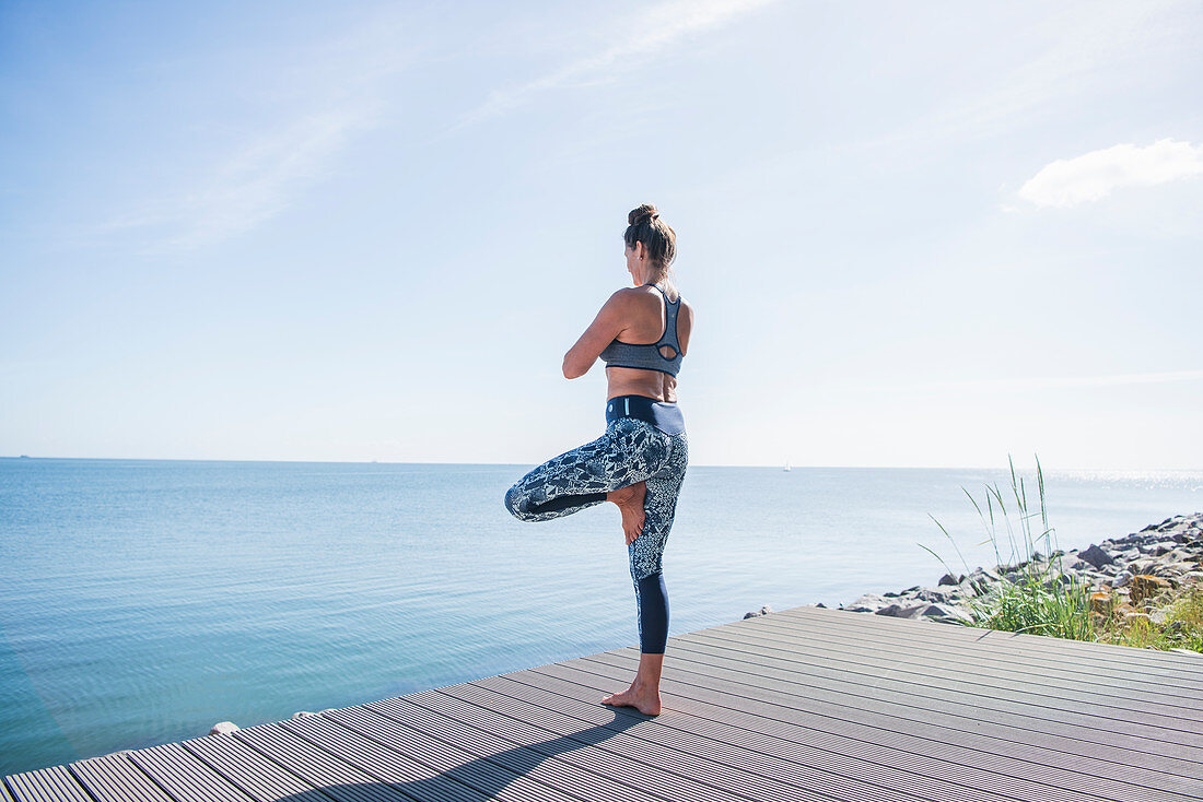 Woman doing yoga (tree pose) next to the sea