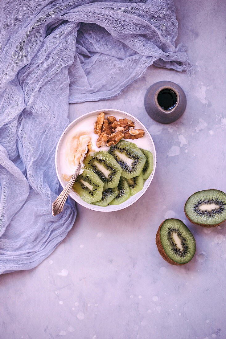 Yoghurt in a bowl topped with maple syrup, fresh kiwi and walnuts