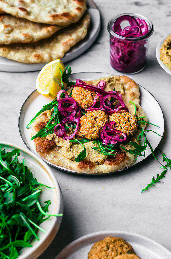 Falafel aus roten Linsen serviert auf Naanbrot mit Hummus und Zwiebeln