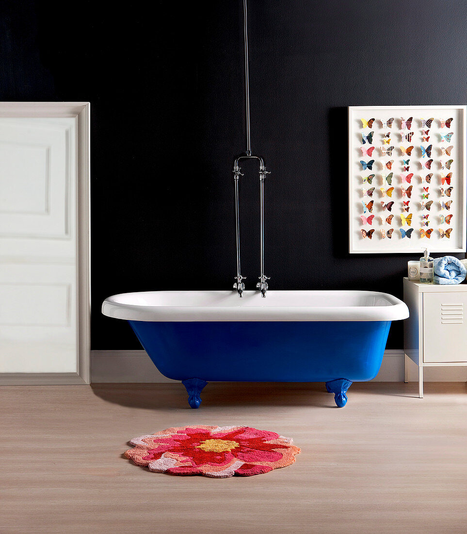 Blue, free-standing bathtub against a black wall, paper butterflies as wall decoration