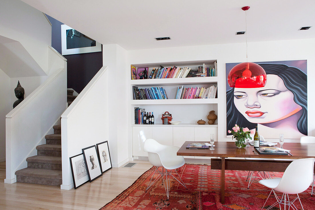 Dining table with shell chairs in front of bookshelf and artwork